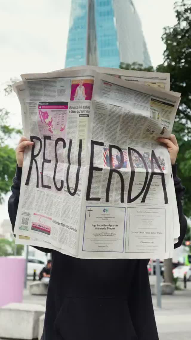 A hand-written newspaper sheet reading RECUERDA held up in the street