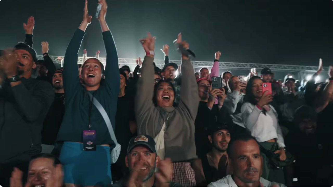 The crowd on their feet; the camera tracks past them and finds an athlete alone in his head