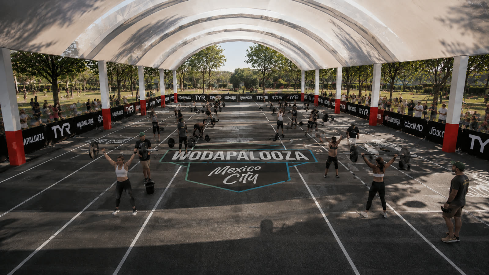 Athletes lifting on the covered outdoor floor beneath its arched canopy